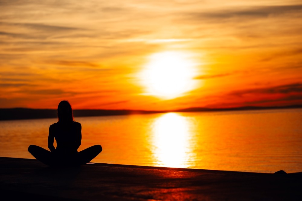 Woman Meditating by the Ocean During Sunset