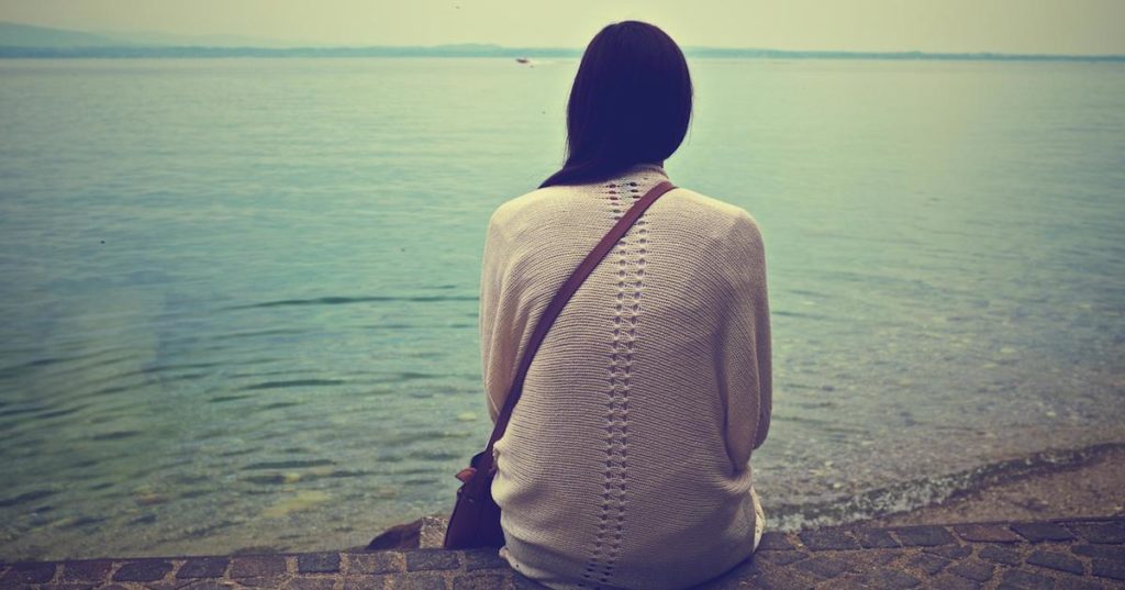 Woman Sitting on Ledge Facing the Ocean