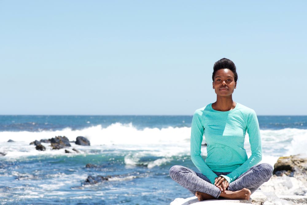 Woman Meditating on Rocks by the Ocean