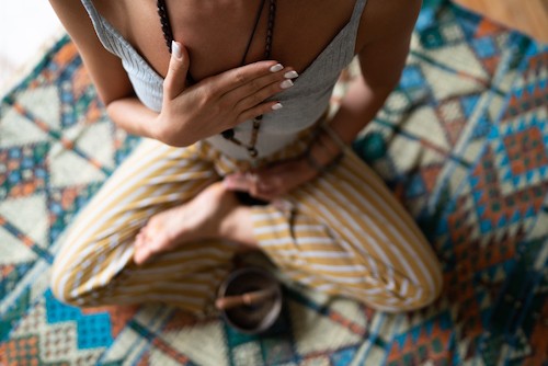 Close-up of a woman's hand on her chest while doing breathing exercises and meditating at home. Caucasian woman sitting in a lotus position, practicing pranayama.